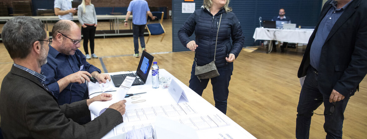 Eine erleichterte Wählerin namens Maria lässt sich den Wahlzettel für die EU-Wahlen aushändigen, obwohl Wahlstellenleiter Povl Kylling Petersen – rechts im Bild – die Wahl eigentlich schon für beendet erklärt hatte.