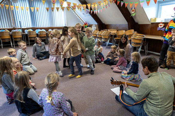 Mehrere Kinder sitzen in einem Kreis zusammen und schauen auf eine Gruppe von fünf Kinder, die im Kreis zusammen einen weiteren Kreis bilden und einmal im Kreis herumgehen.